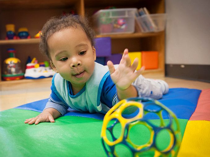 A toddler reaches for a ball while at daycare.