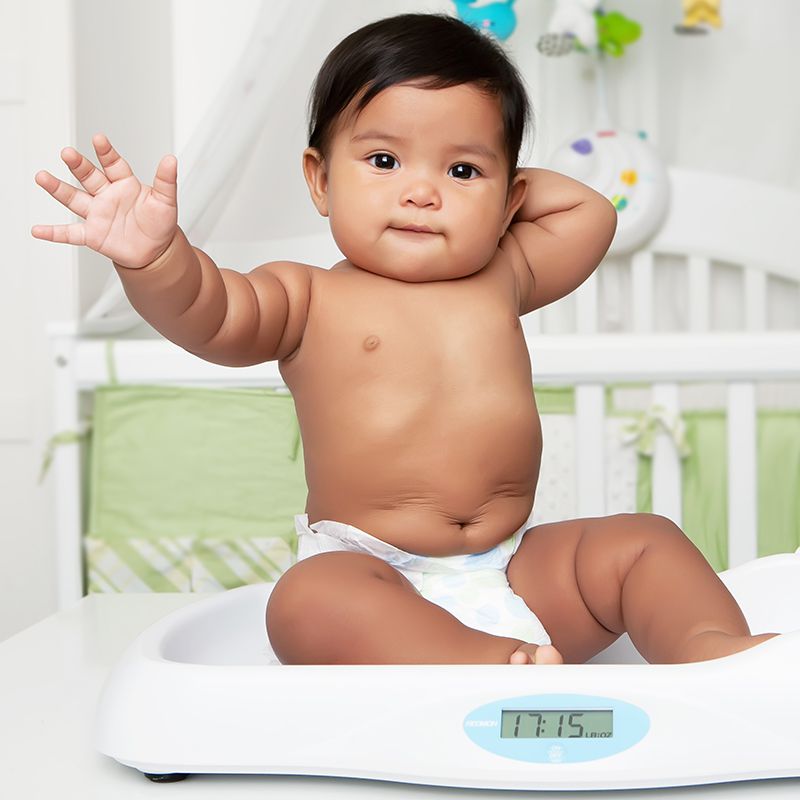 A baby waves while being weighed