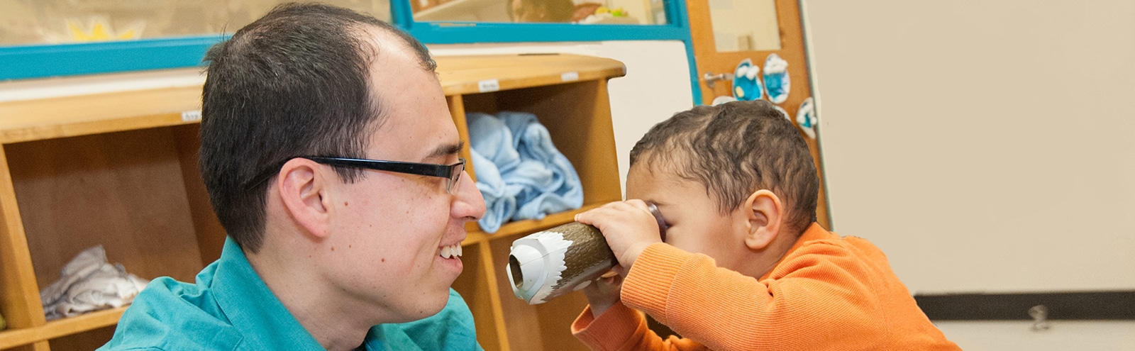 Un niño mira a un educador de primera infancia a través de binoculares de juguete.
