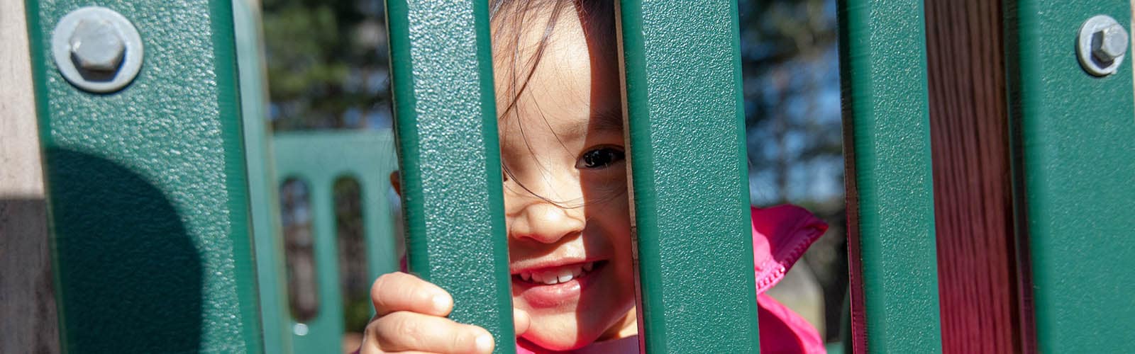 Una niña mira a través de un objeto en el patio de juegos y sonríe.