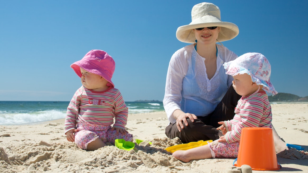 Mother on beach with two young children, all wearing hats and long sleeves