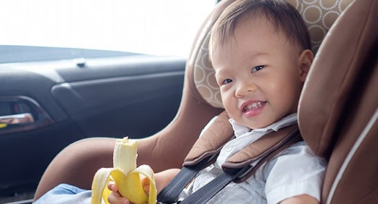 Child in a car seat eating a banana