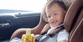Child sitting in safety car seat holding banana