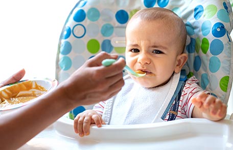 Baby in highchair reacts negatively to baby food.