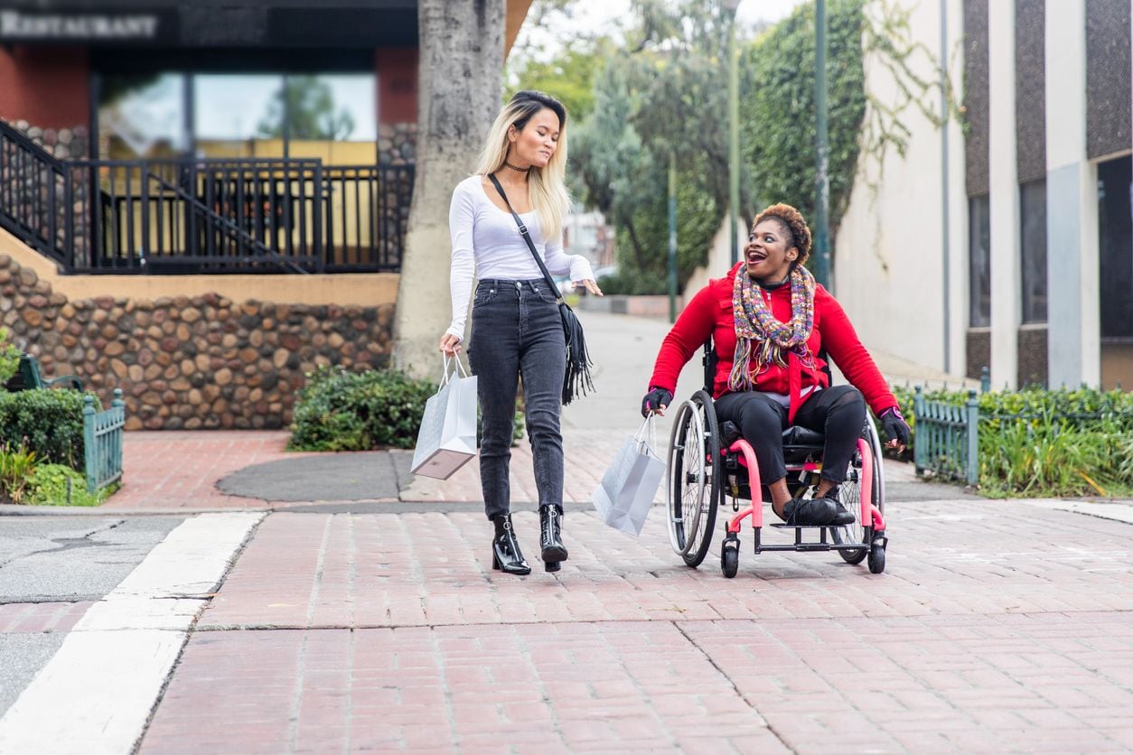 A woman in a wheelchair and a woman walking across the street