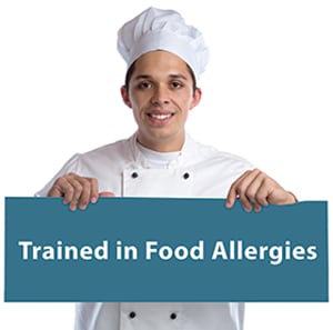 Photo of a chef holding a sign that reads Trained in Food Allergies.