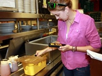 A woman taking the temperature of food in a restaurant kitchen.