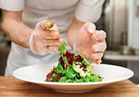 Photo of hands with gloves on preparing a salad on a plate.