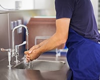 Kitchen staff person washing hands at sink.