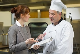 Female kitchen manager discussing a list with a chef.