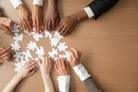 Hands of multi-ethnic team assembling jigsaw puzzle representing teamwork.