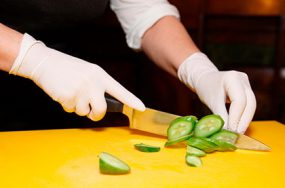 Photo of gloved hands chopping a cucumber.