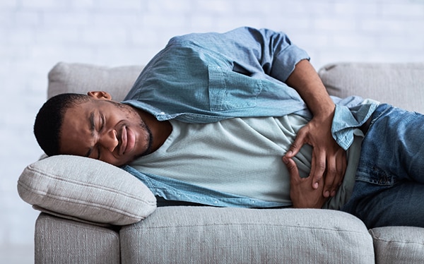 Man suffering from abdominal pain lying on sofa indoor