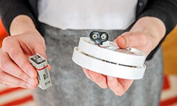 A person replacing a battery in a carbon monoxide detector