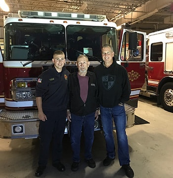 Tres generaciones de bomberos de Michigan en la estación de bomberos frente a un camión de bomberos.