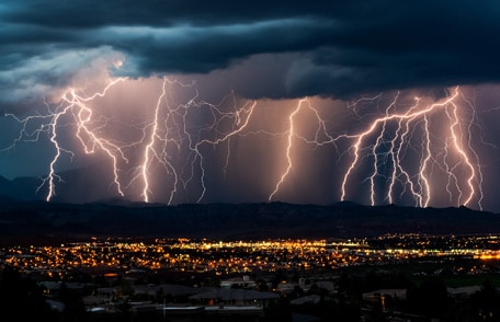 Multiple streaks of lightning touch ground as a large storm passes over a city.