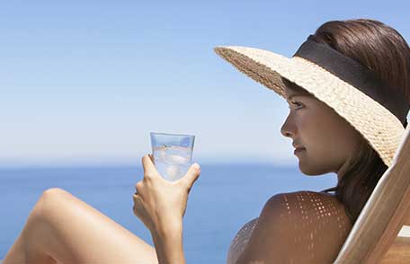 A woman wearing a brimmed hat and drinking cold water on the beach.