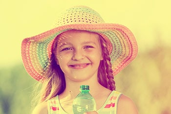 a young girl wearing large brim hat and drinking a bottle of water