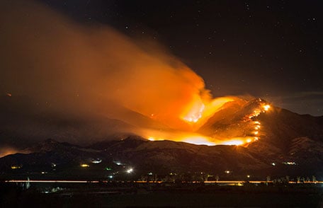 Wildfire burning on the side of a large hill at night.