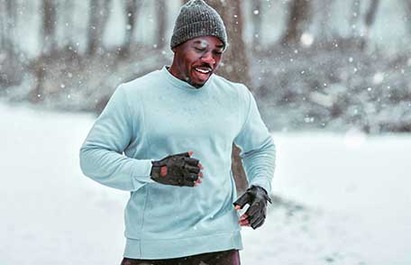 A man wearing gloves and a knit cap jogs down a snowy path.
