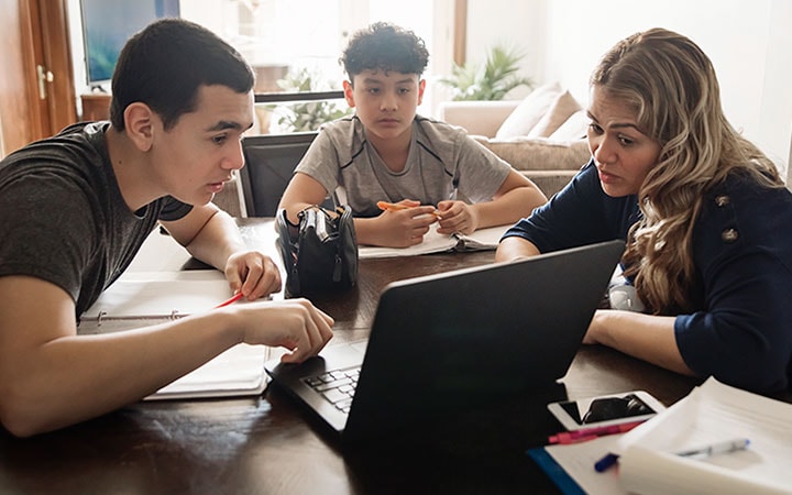 Three teens sitting at a table in front of a laptop doing research.