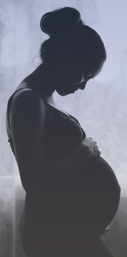 Profile of a pregnant woman looking down and holding her belly.