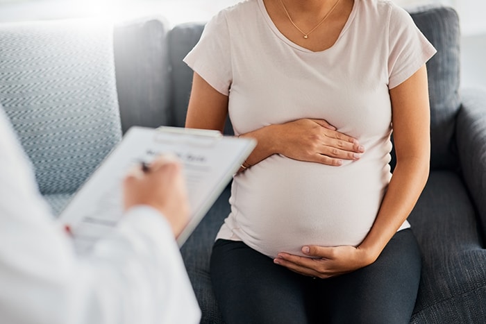 Pregnant woman holding her belly while speaking with a doctor.