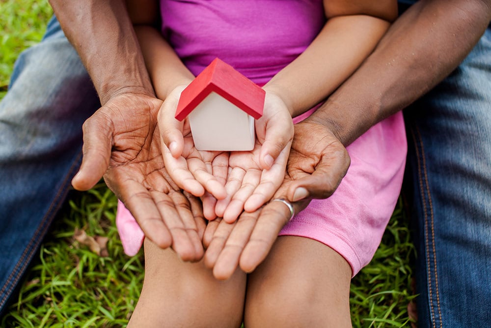 Adult and child holding a house in their hands.