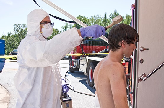 Young man being washed down in a decontamination wash station with suited health worker