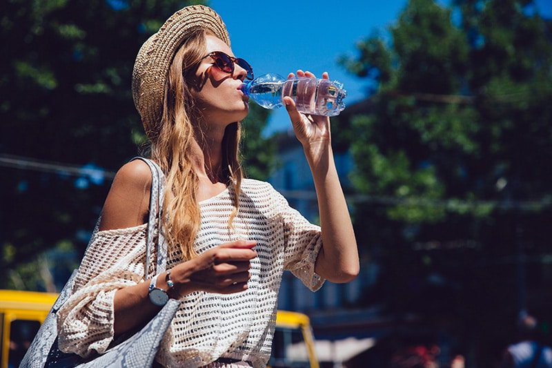 A woman drinking a bottle of water in the sun.