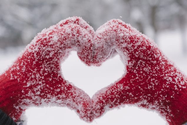 Hands in red mittens making a heart shape while snowing outside
