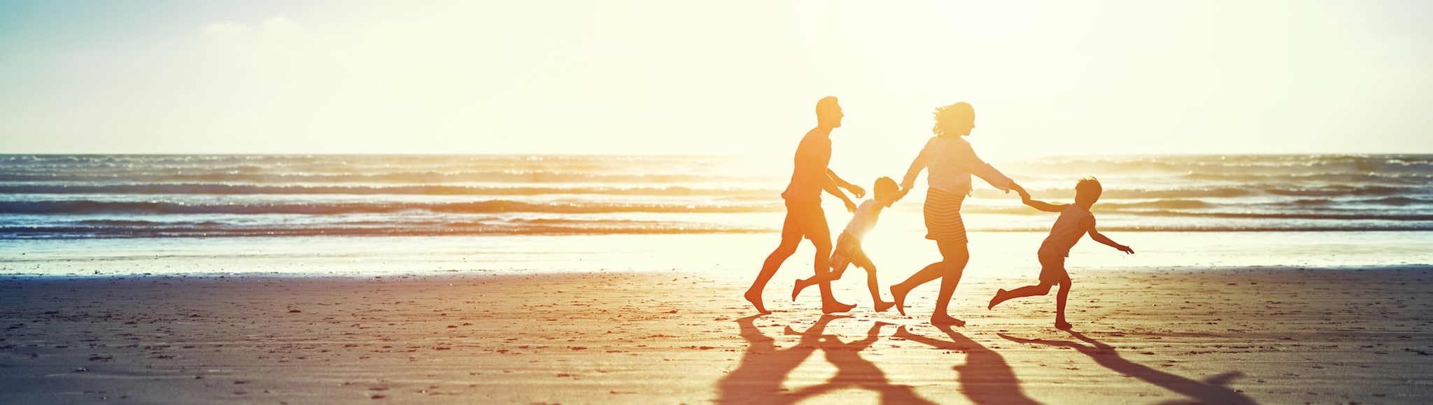 Family walking on beach holding hands, in silhouette from sunset