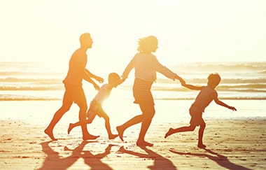 Family running hand-in-hand on beach at sunset