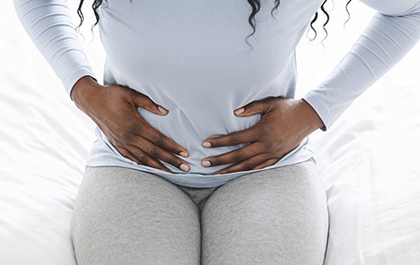 African american woman suffering from stomach ache, holding belly on edge of bed.