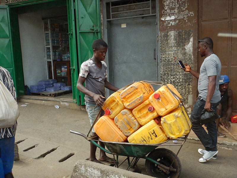 A young man hauls plastic containers in a wheelbarrow down an urban street