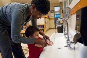 Day care worker helping a toddler wash his hands with soap and warm water