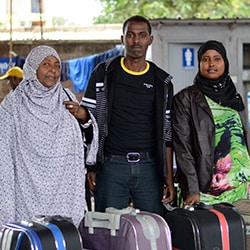 A mother and her two children stand behind their suitcases.