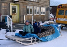 People on dogsled in front of building