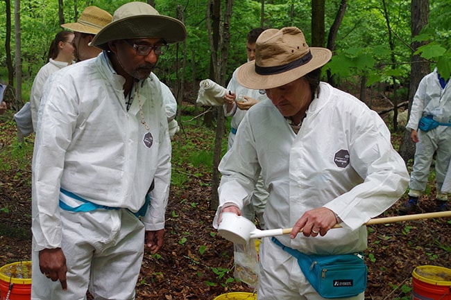 Two persons wearing personal protective gear observing a mosquito dip in the woods. 