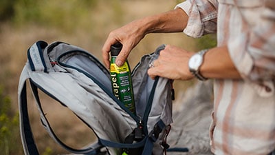 A person putting a can of insect repellent into a backpack.