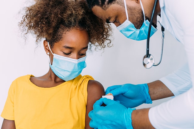 Un médico le pone una curita en el brazo a una niña que recibió la vacuna.