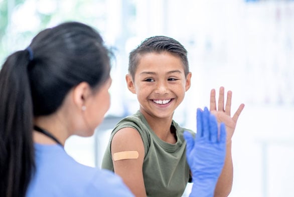 Una proveedora de atención médica saluda a un niño que tiene una curita en el brazo después de recibir la vacuna.