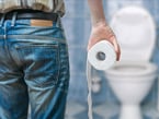 Image of man from behind holding a roll of toilet paper, facing a toilet in the background