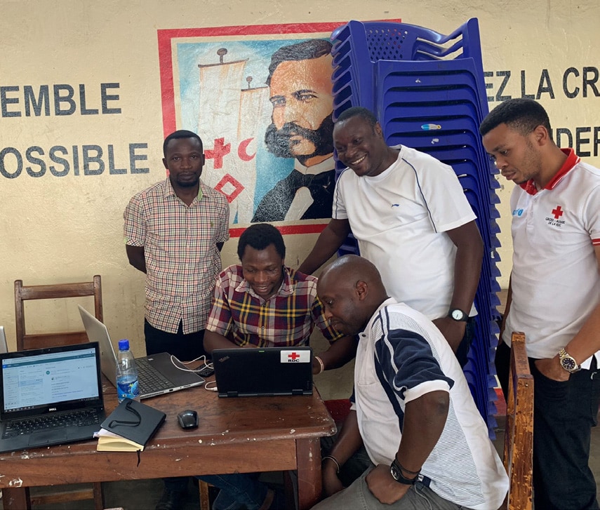 Red Cross volunteers look at community feedback data to help them strengthen outreach efforts—with inspirational message in background, 'Together, it is possible.'