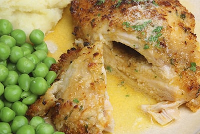 Image shows a plate with a plate with a stuffed chicken breast, green peas and mashed potatoes