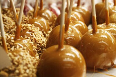 Image shows a tray of shiny caramel apples with and without peanuts