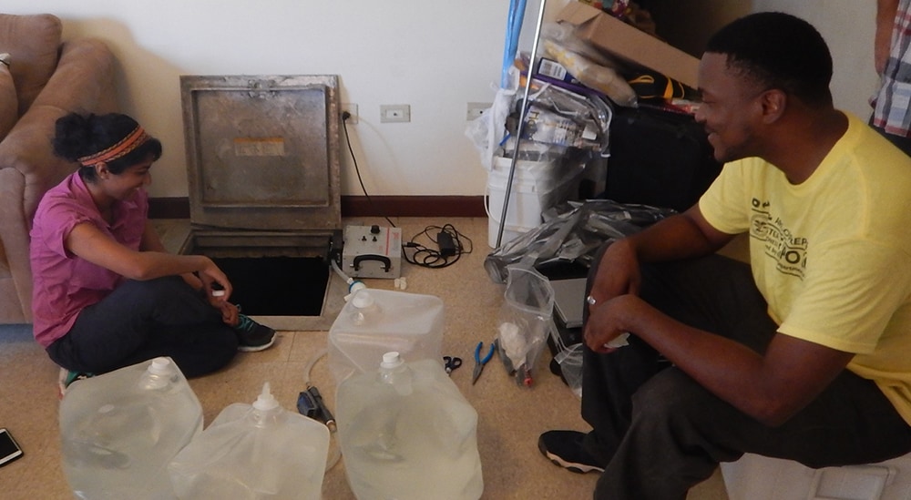 Gouthami Rao (DFWED) and Kaunda Williams (VIDOH) oversee the collection of a water sample from a household cistern to test for evidence of waterborne pathogens.