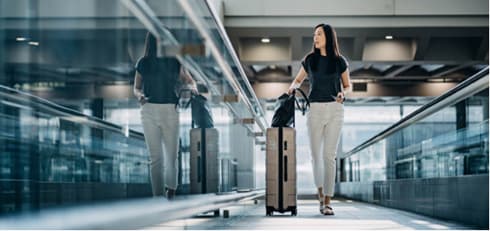 A woman walking her luggage in an airport.