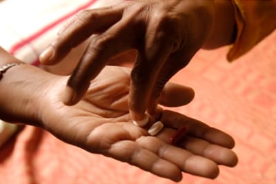 An image showing one hand placing a pill into someone's palm