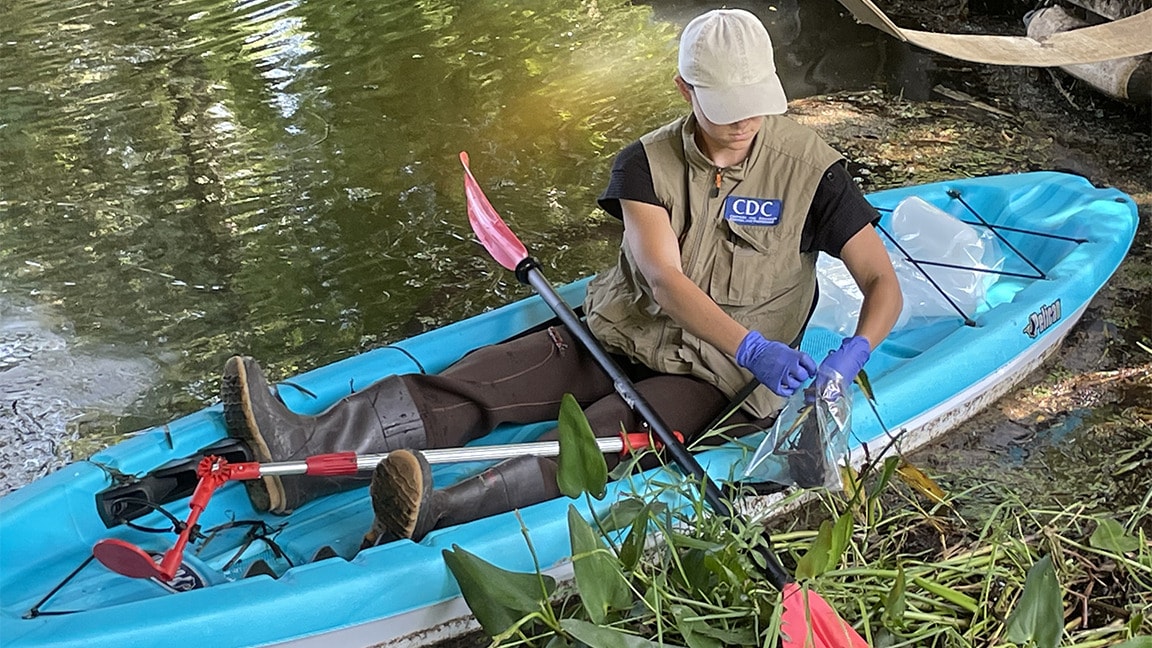 A woman wearing a CDC vest collects water samples in a kayak